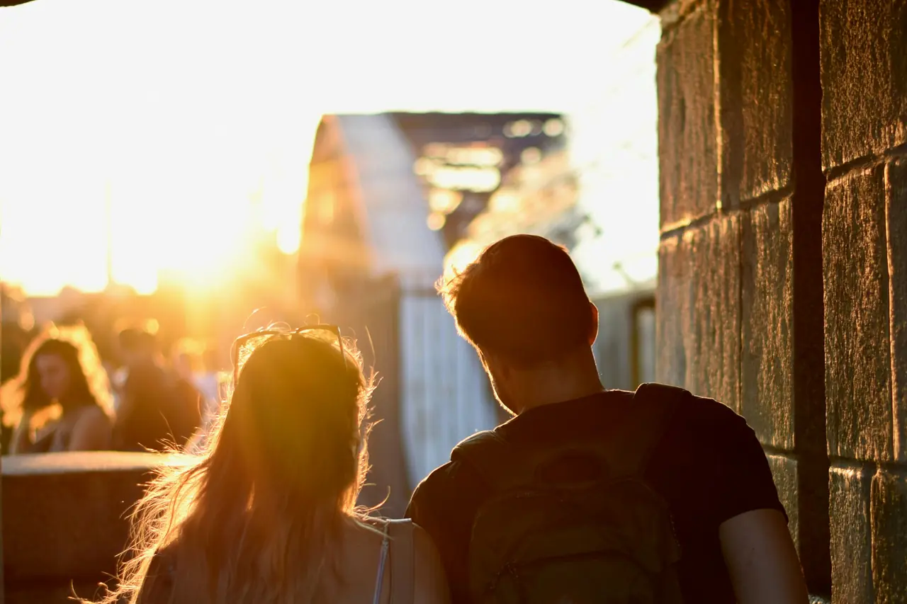 A couple seen from behind, lit by golden evening sun on a bridge