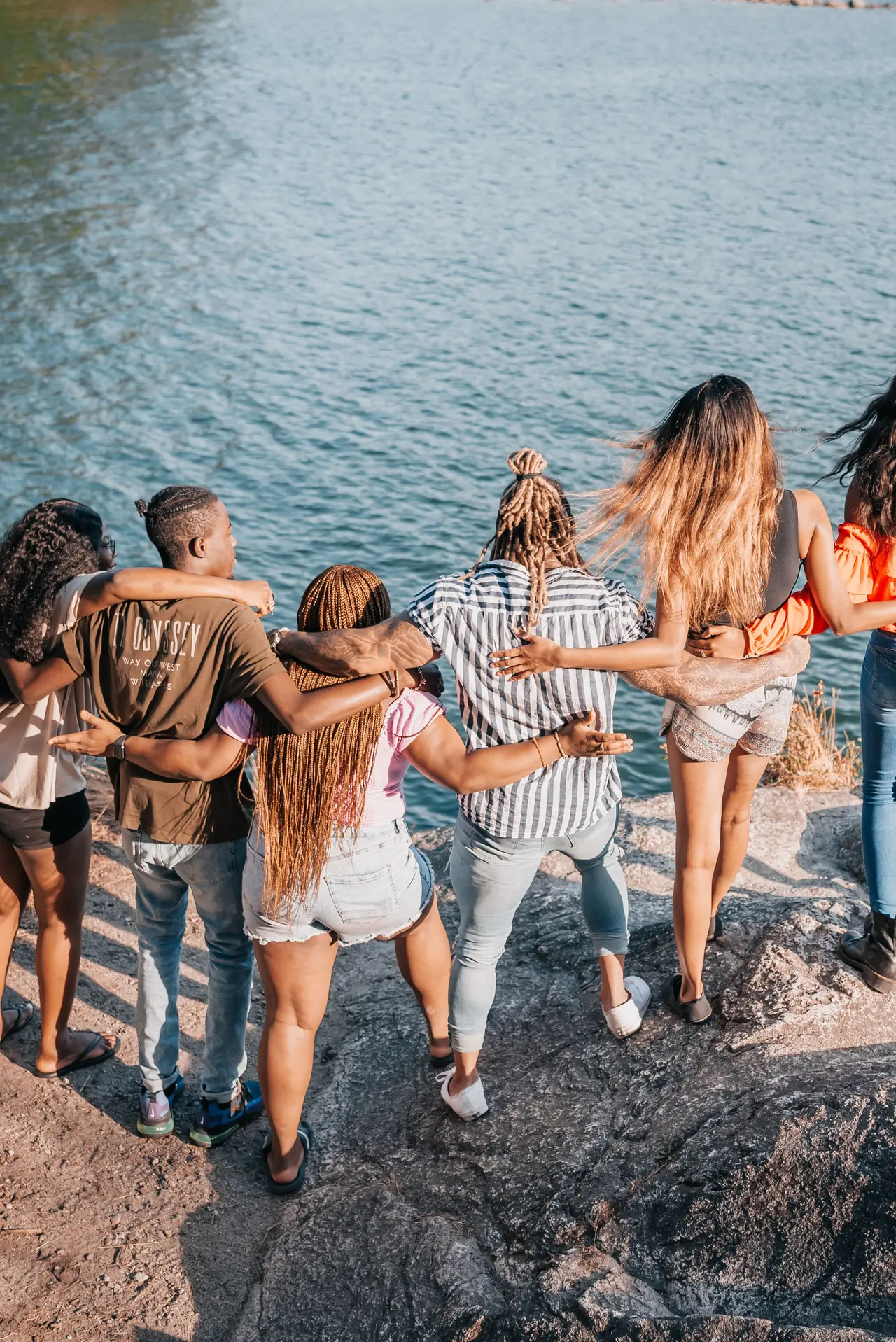 Friends walking arm in arm along a rocky lakeshore